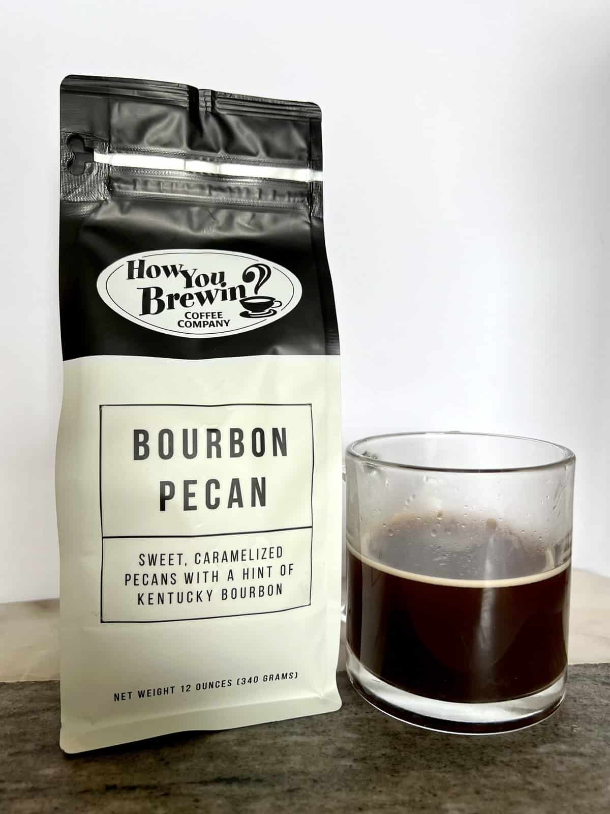 a-package-of-Bourbon-Pecan-coffee-stands-next-to-a-brewed-cup-of-coffee-scaled