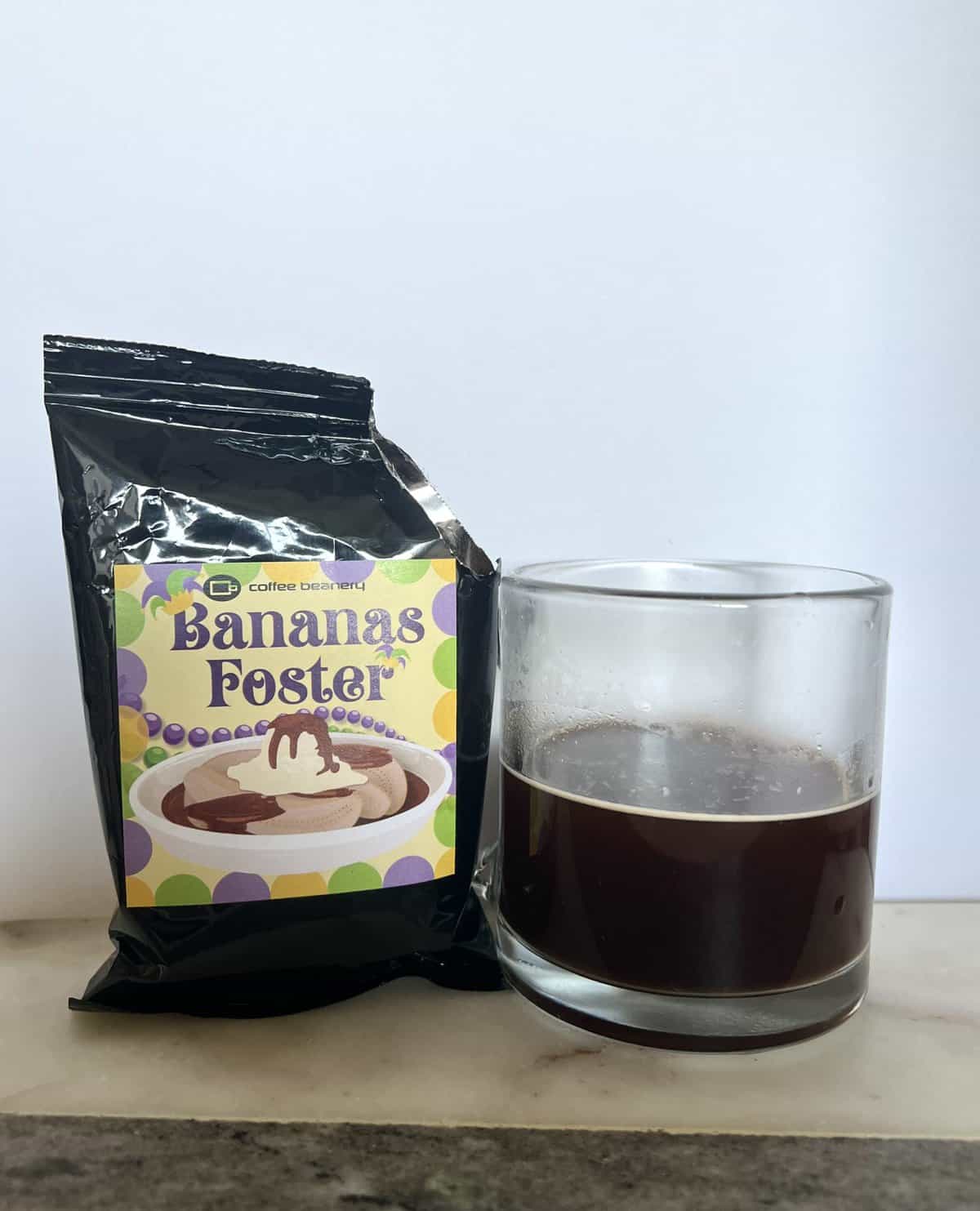 open-package-of-coffee-beanery-Bananas-Foster-next-to-a-cup-of-brewed-coffee-scaled